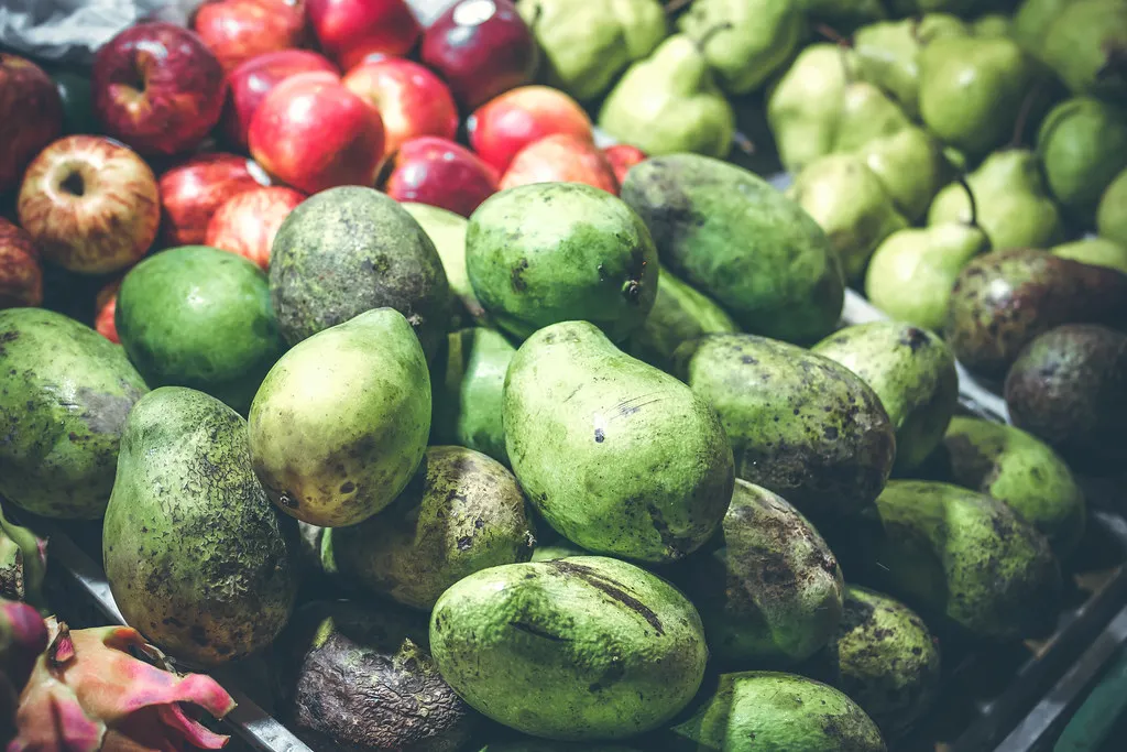 Piles of green tropical fruit and red apples on a market stall
